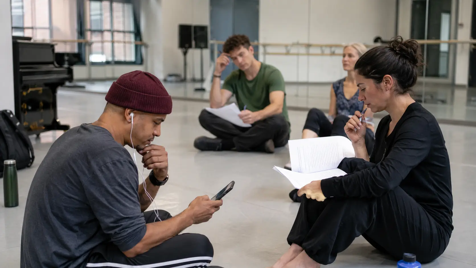 Performers reviewing rehearsal material while one person listens to an audio copy on a phone.