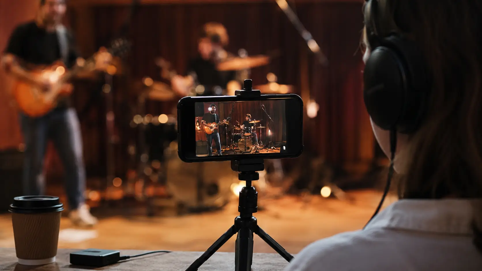 An iPhone recording a live band performance while a listener monitors the sound through headphones.