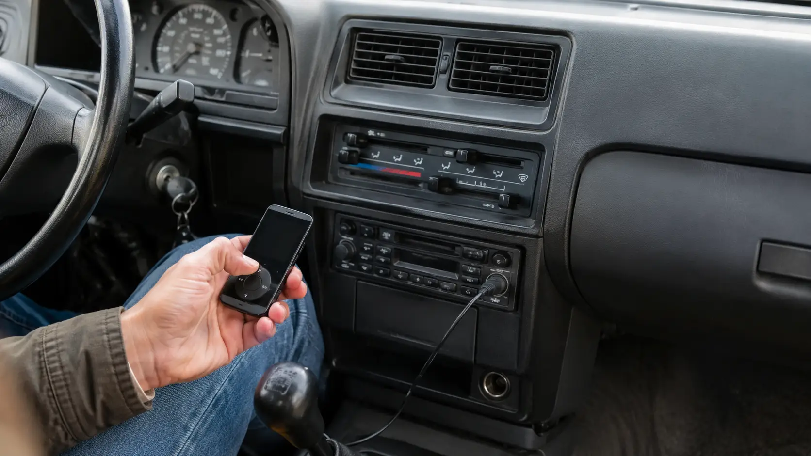 A portable audio player connected to an older car stereo for music playback.